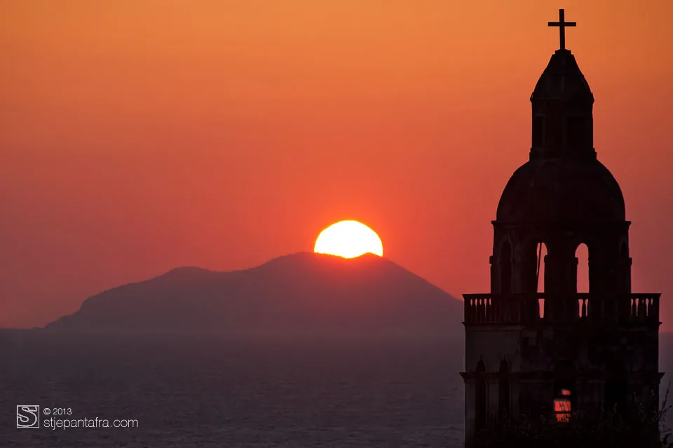 Un campanile contro il sole che tramonta nel mare